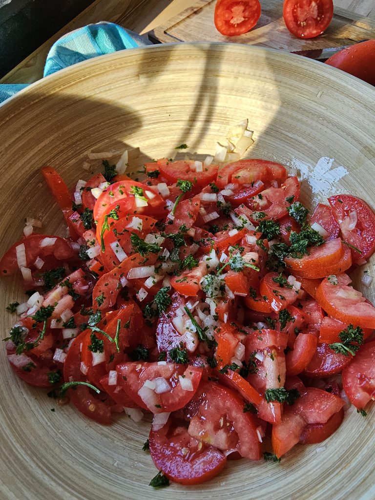 Klassischer Tomatensalat mit frischen Tomaten, Zwiebeln, Petersilie und Essig-Öl-Dressing in einer rustikalen Holzschüssel